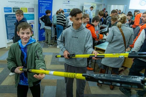 A képen két fiú látható, akik egy sárga, teleszkópos eszközt tartanak