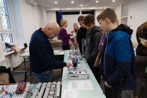 A képen egy felnőtt férfi látható, aki egy asztalon elhelyezett elektronikai áramköröket mutat be